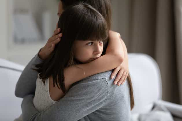 A little girl hugging a woman and lookin gsadly out over her shoulder-2